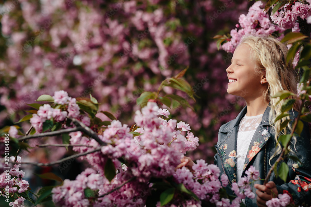 Fototapeta premium portrait of a beautiful little child girl with sakura flowers on a sunny spring day