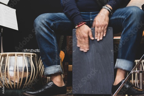A stylish musician in denim and double monk shoes plays the Cajon, a Peruvian drum used commonly with Spain’s Flamenco dance.  photo