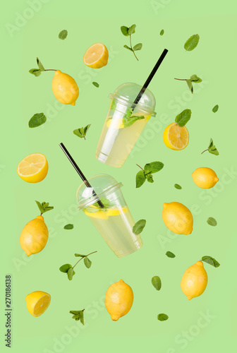 Flying refreshing lemonade from a plastic cups with flying lemons & mint leaves on a green background. Jar full of cold cocktail. Fresh concept. Mock up.