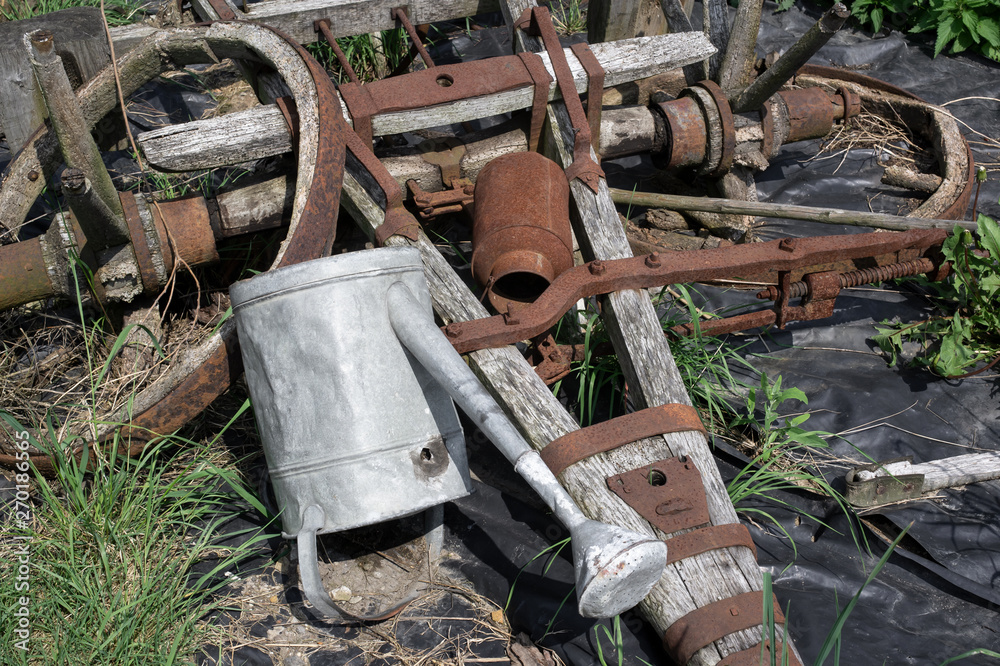 Rustic equipment from rural farm is corroded and rusty. Wheel, watering can and wooden cart /wagon / plough. History and nostalgia. Rustic equipment from rural farm is corroded and rusty. Wheel, watering can and wooden cart /wagon / plough. History and nostalgia.