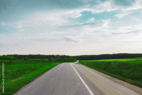 asphalt road through the green field and clouds on blue sky in summer day