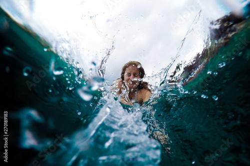 Young woman dives into the water. View from under the water, spray. Summer holiday concept, jump to the pool