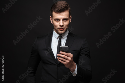 Business man posing isolated over black wall background using mobile phone.
