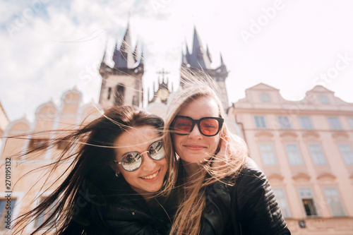 Girls, best friends are walking around Prague. Blonde and brunette enjoy traveling in Prague in the background Old Town Square. Closeup portrait. photo