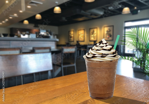 Frappuccino with cream and chocolate sauce in takeaway cup on wooden table at cafe photo