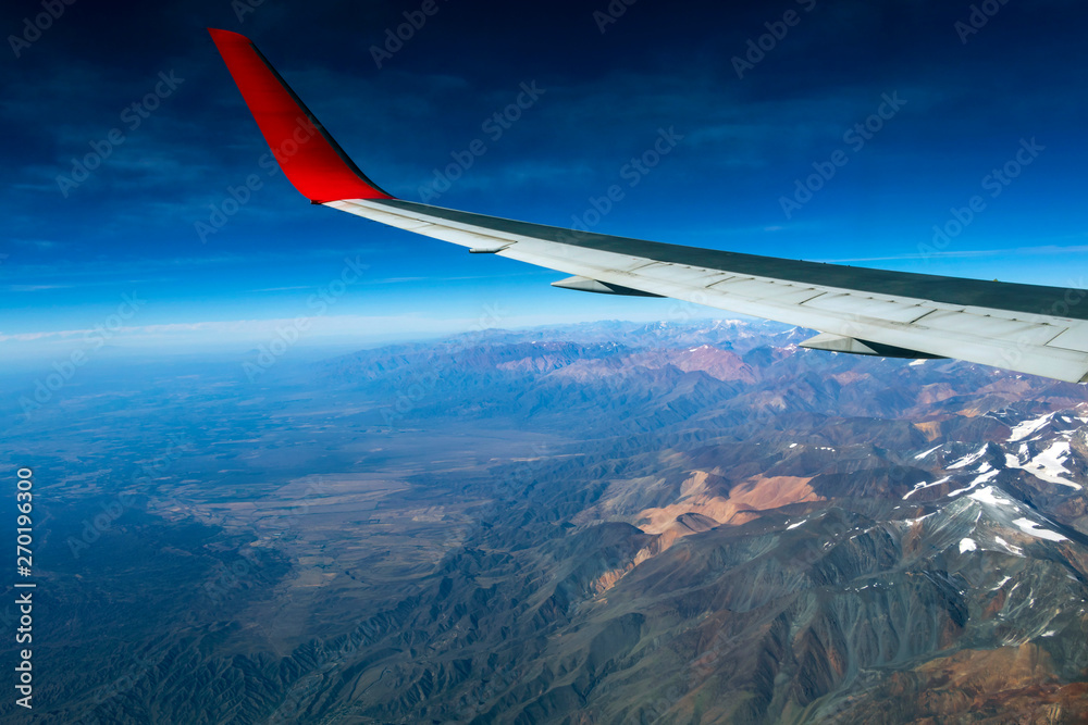 Wing of an airplane flying above the morning clouds and Andean mountain range Wing of an airplane flying above the morning clouds and Andean mountain range
