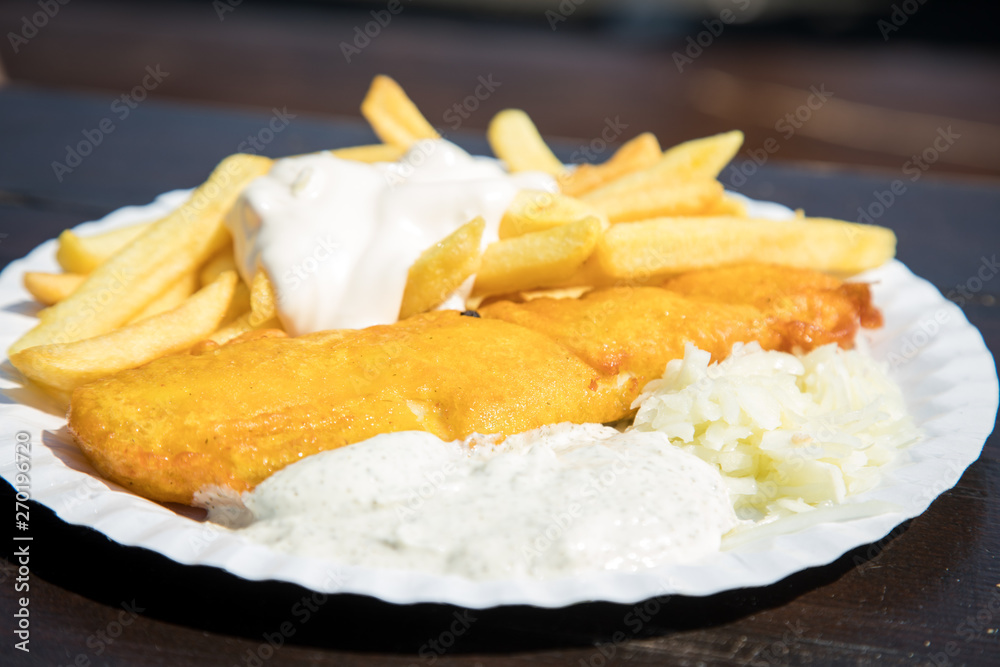 Seelachs Backfisch im Bierteig mit Remoulade, Pommes, Mayonnaise und Krautsalat draußen auf Pappteller und Holztisch Seelachs Backfisch im Bierteig mit Remoulade, Pommes, Mayonnaise und Krautsalat draußen auf Pappteller und Holztisch