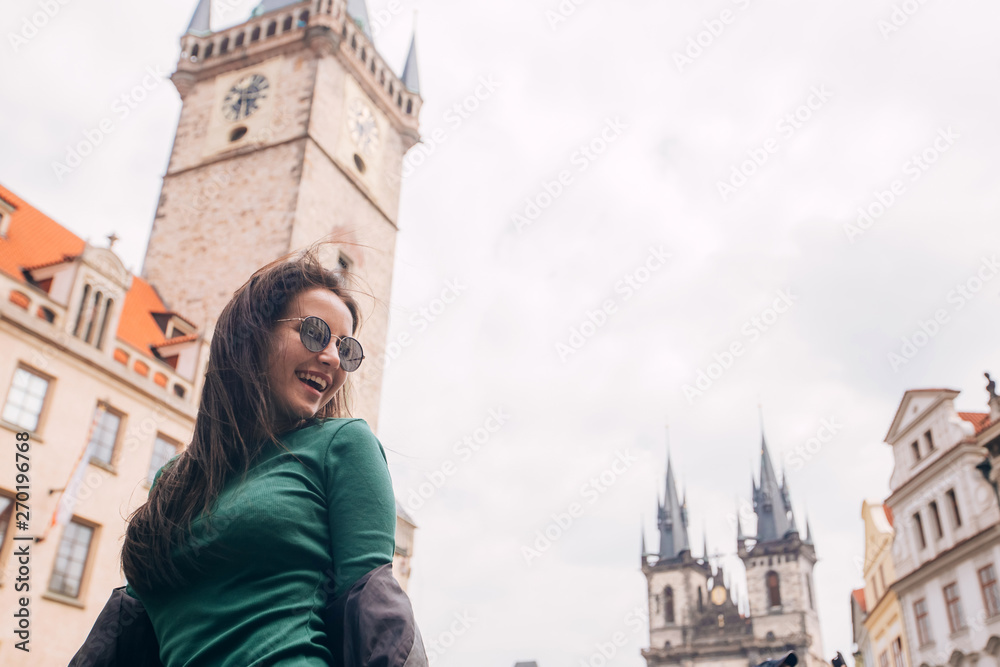 Fototapeta premium Street portrait of adorable brunette woman in sunglasses posing at Old Town Square in Prague. smiling pretty brunette girl, lifestyle. Old Town Hall with astronomical clock tower in Prague, Czech