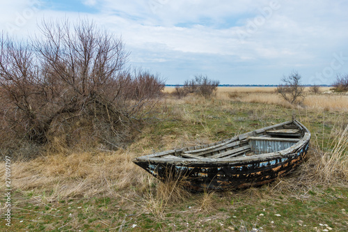 The old abandoned wooden fishing boat among dry brown grasses