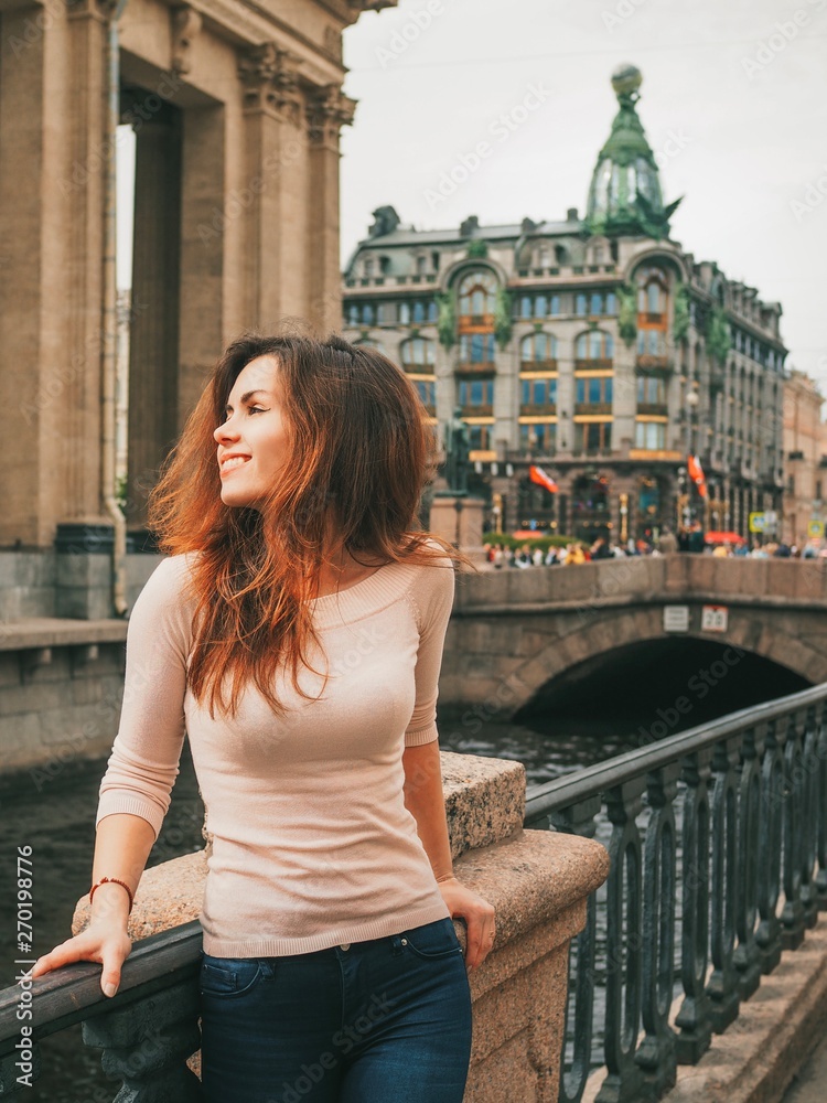 Brunette girl with long hair stands  on the streets in the center of St. Petersburg near the canals on the background of the Kazan Cathedral
