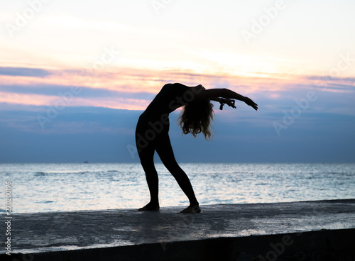 unrecognizable senoir woman with beautiful body doing yoga at sunrise on the sea  silhouette of yoga poses
