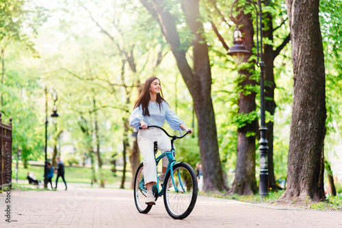 Happy smiling girl with long hair riding a blue bicycle in a city park on a sunny day © WellStock