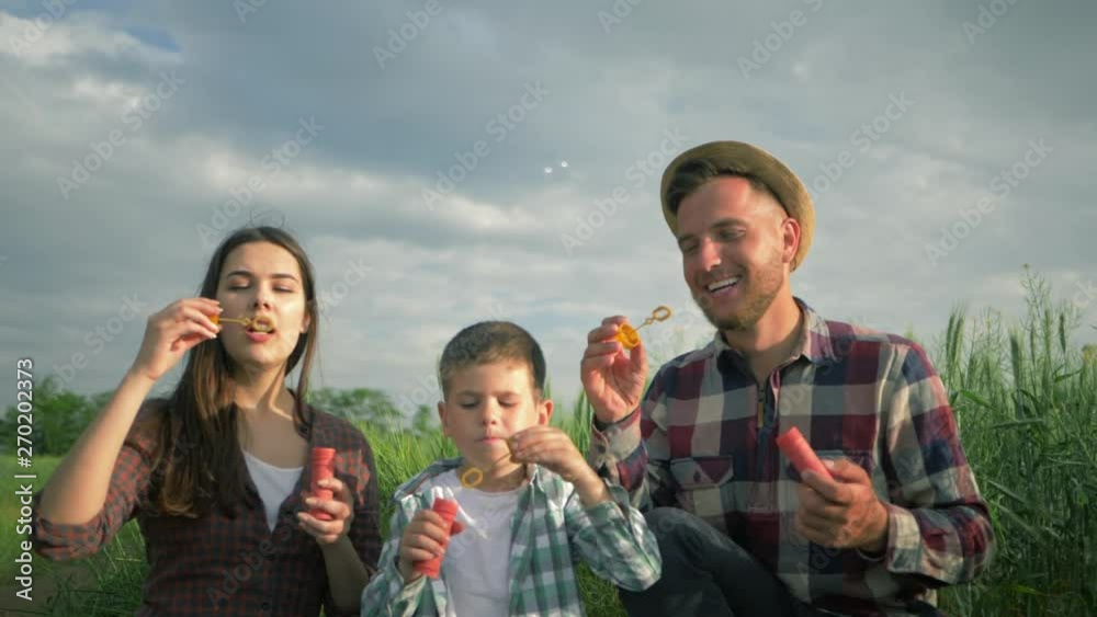 family blowing soap bubbles and laughing in slow motion, little boy with mum and daddy in plaid shirts have fun during weekend at green meadow family blowing soap bubbles and laughing in slow motion, little boy with mum and daddy in plaid shirts have fun during weekend at green meadow