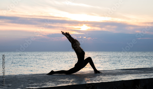 unrecognizable senoir woman with beautiful body doing yoga splits at sunrise on the sea, silhouette of yoga poses photo