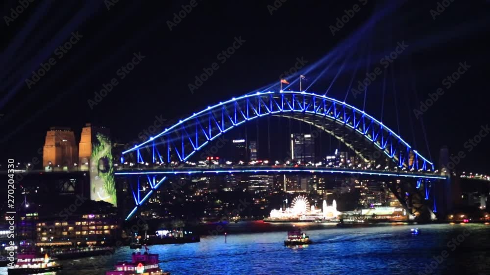 Bright colours on the arch of Sydney Harbour bridge over waters of Harbour at night with blue laser beams of Vivid Sydney light show. Bright colours on the arch of Sydney Harbour bridge over waters of Harbour at night with blue laser beams of Vivid Sydney light show.