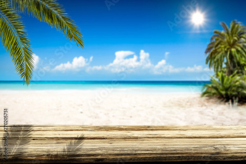 Wooden table background of free space and summer landscape of beach with palms and ocean. 