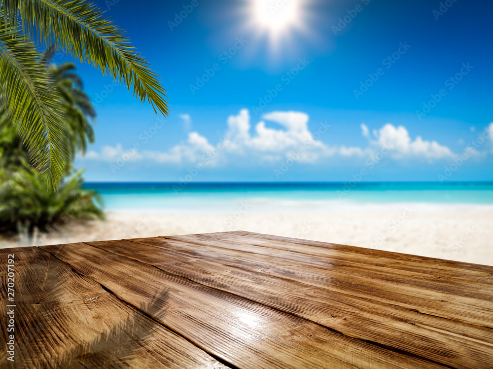 Fototapeta premium Wooden table background of free space and summer landscape of beach with palms and ocean.