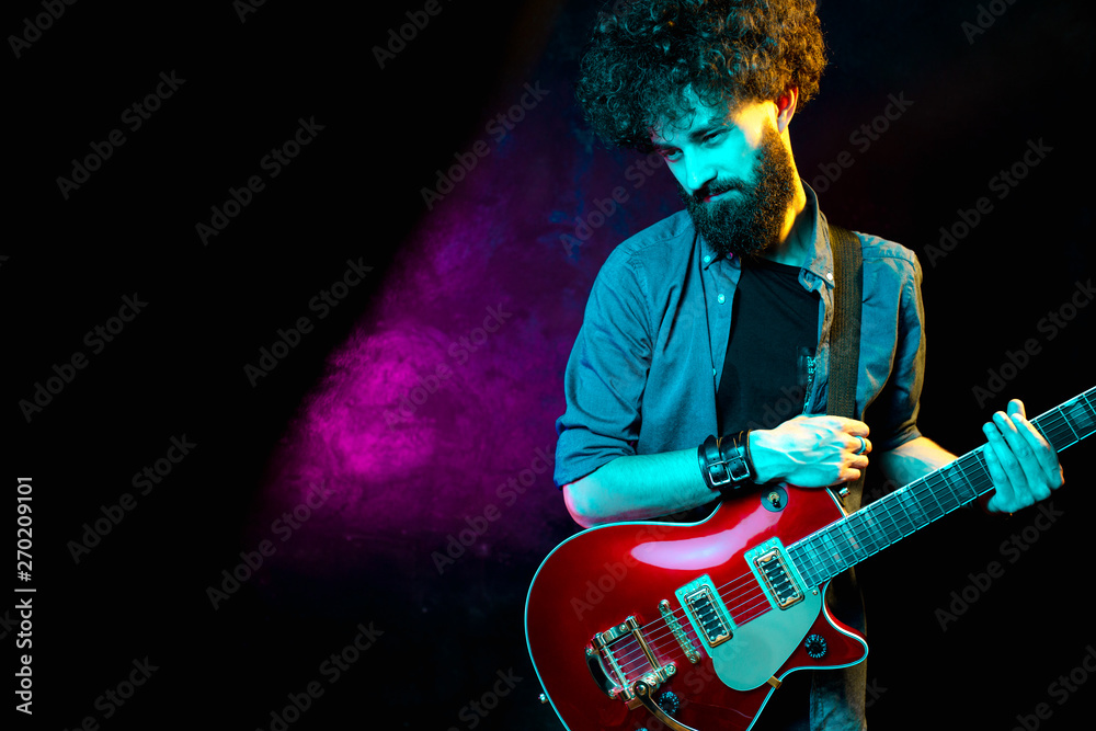 Obraz premium Close-up photo of hipster man with red guitar in neon lights. Rock musician is playing electrical guitar.