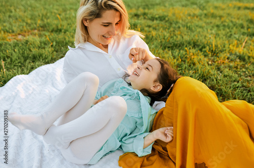 Happy litttle girl playing and having fun with her mother on white blanket at the green grass. Mom and kid shares love. Mother and daughter enjoying time together in the park. Childhood and motherhood © iuricazac