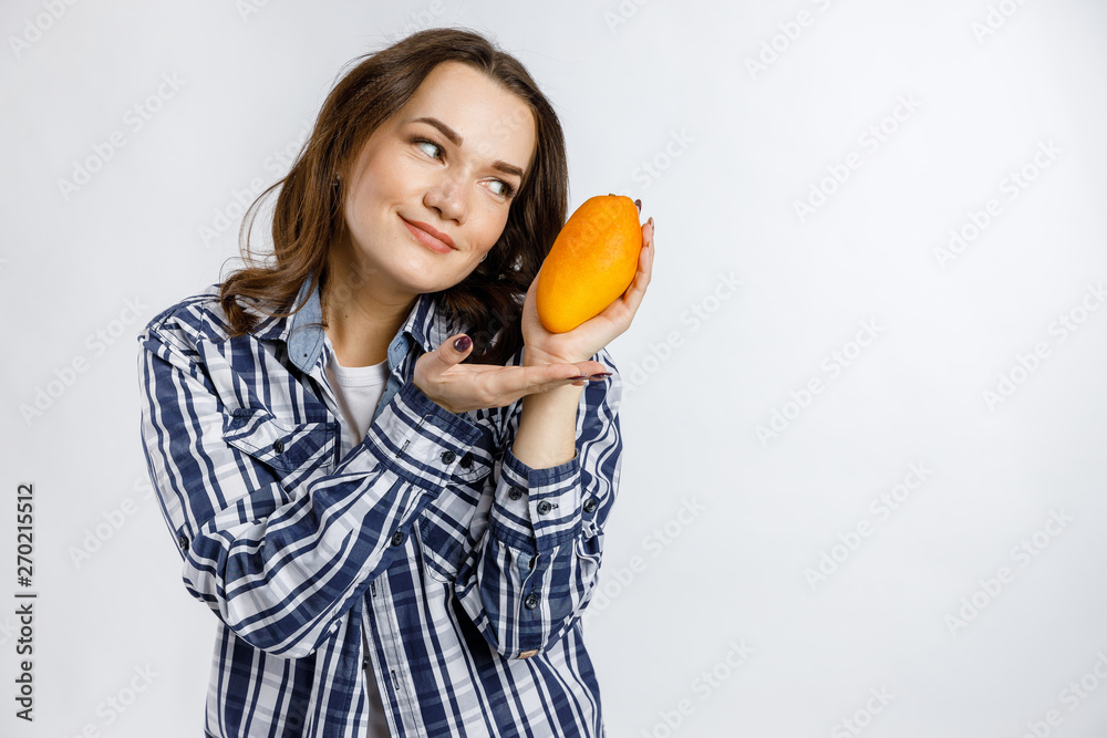Young beautiful girl in plaid shirt holding mango on white background. Healthy food - vegetables, fruits and berries. Young beautiful girl in plaid shirt holding mango on white background. Healthy food - vegetables, fruits and berries.