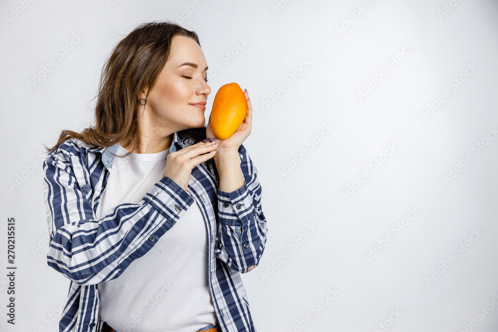 Young beautiful girl in plaid shirt holding mango on white background. Healthy food - vegetables, fruits and berries. Young beautiful girl in plaid shirt holding mango on white background. Healthy food - vegetables, fruits and berries.
