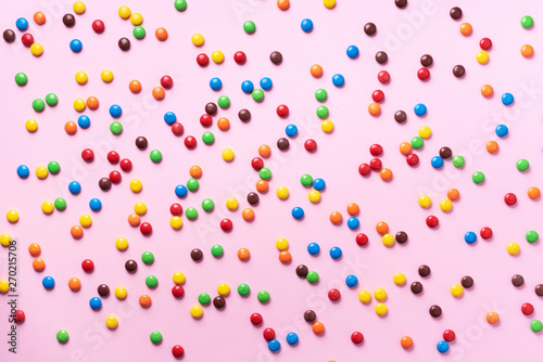 Rainbow colorful candies on pink background. Coated chocolate sweet pieces texture. Top view. Flat lay. Confetti for holidays, birthday party concept