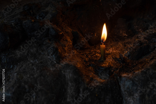 A taper is burning in a cave amidst stones in the dark. burning candles on the stones