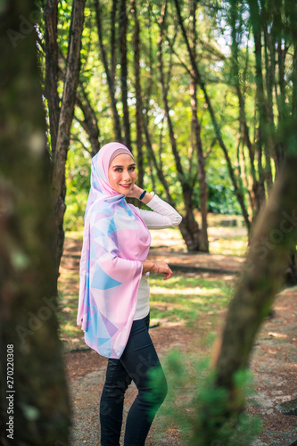Young attractive Muslim Malay woman, modern contemporary fashion in hijab, close up portrait face and body, blurred background smiling and happy at park.