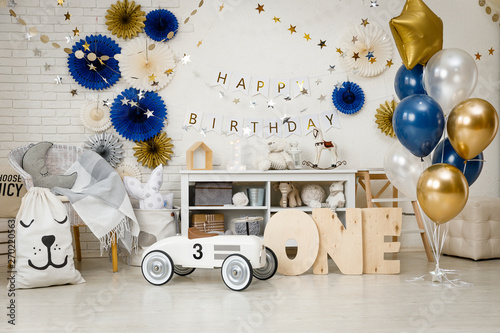 Birthday decorations with gifts, toys, garlands and figure for little baby party on a white bricks background. 