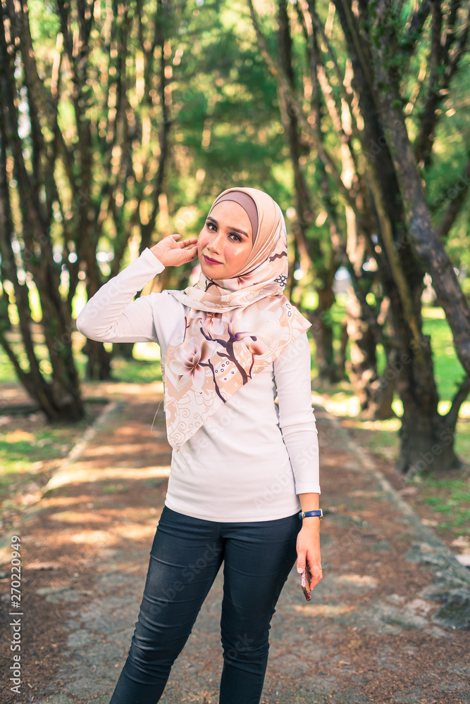Portrait young attractive Asian Muslim woman, smile and happy face, at green park. New modern, contemporary casual fashion in hijab, classic and vintage summer warm look. Copy space for advertising. Portrait young attractive Asian Muslim woman, smile and happy face, at green park. New modern, contemporary casual fashion in hijab, classic and vintage summer warm look. Copy space for advertising.