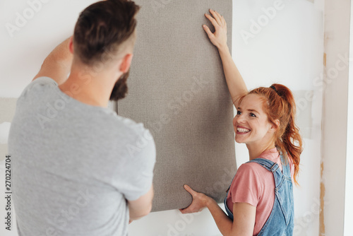 Happy young woman holding up a roll of wall paper