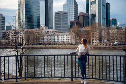 Beautiful young girl with long straight hair standing near skyscrapers and river in Frankfurt am Main, Germany