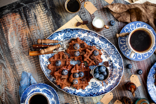 Overhead shot of homemade yummy chocolate waffles on vintage plates with blue ornament stands on wooden dark table © Марина Долбус