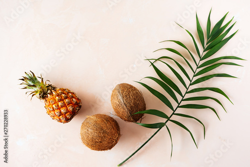 Summer concept with palm leaf, pineapple and hree Fresh Tropical fruit coconut in shell, on pink pastel background with copy space. Simple tropical mood.
