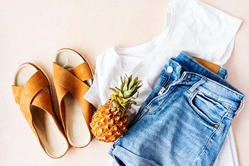 Woman's casual summer vacation outfits with white t-shirts, denim shorts, trendy leather sandals, with crisscross details on pink pastel background. Flat lay.