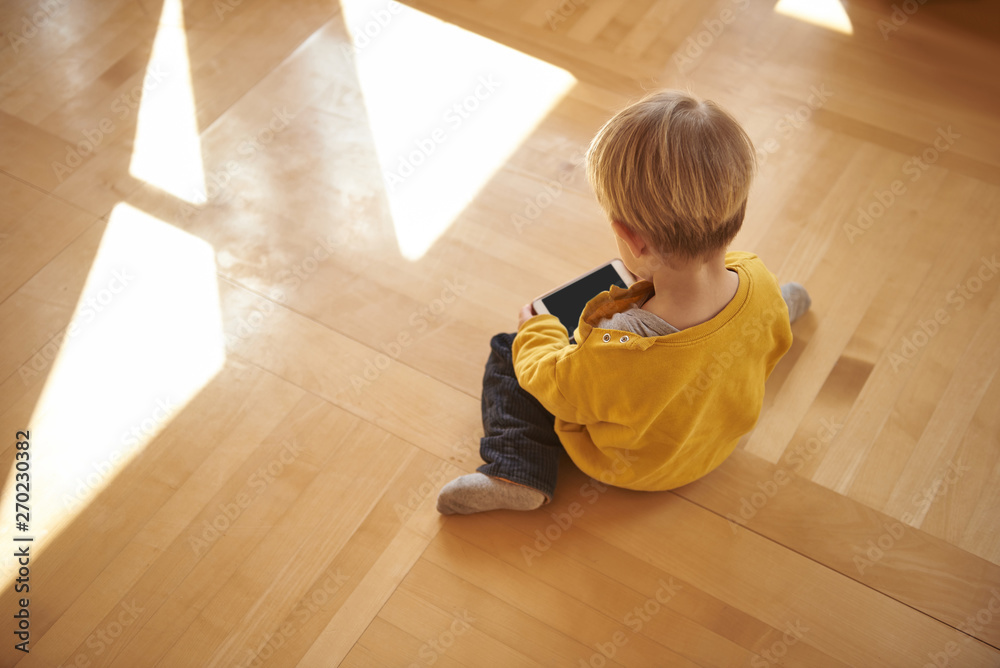 Cute little boy sitting on the floor and using cellphone
