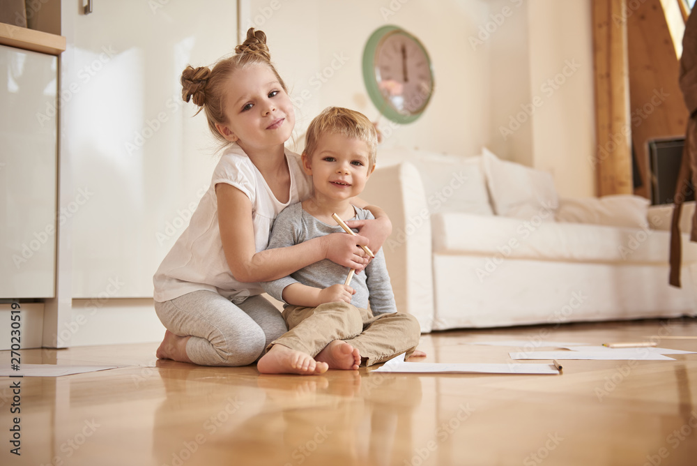 Adorable little girl hugging her brother from behind at home Adorable little girl hugging her brother from behind at home