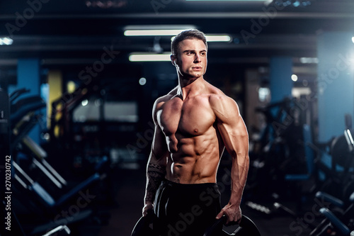 Side view of a caucasian handsome fitness model posing in the gym. Man on diet flexing muscles and six pack abs