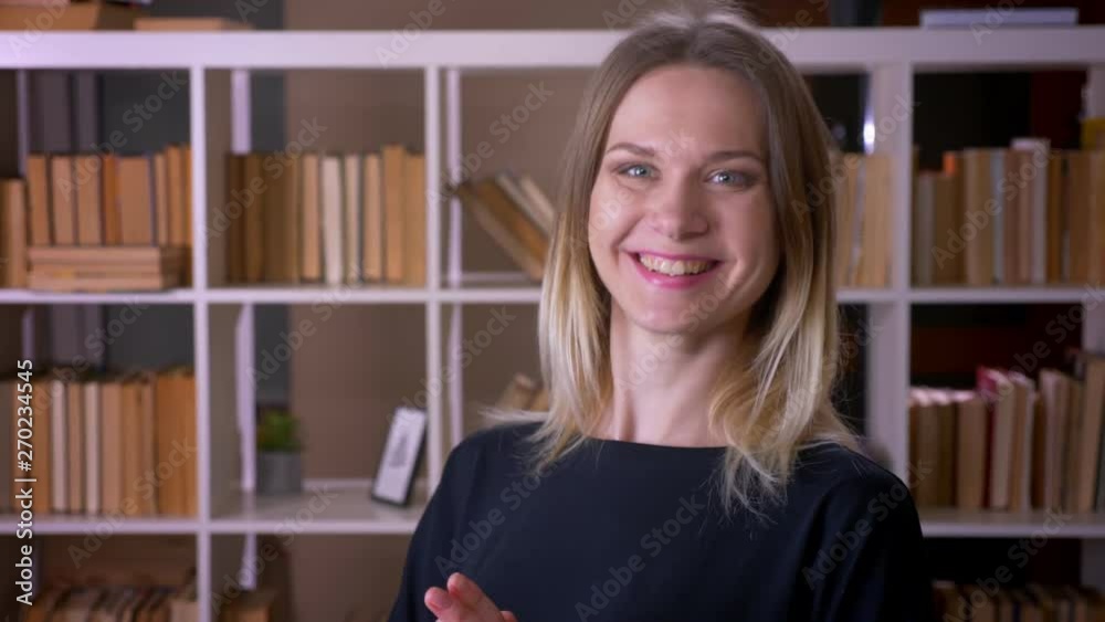 Closeup shoot of young attractive female student turning and looking at camera smiling cheerfully indoors in the university library Closeup shoot of young attractive female student turning and looking at camera smiling cheerfully indoors in the university library