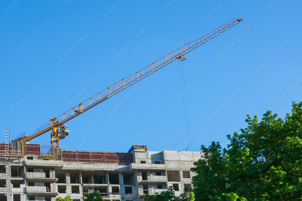 High-rise building crane with a long arrow of yellow color against the sky above a concrete building under construction High-rise building crane with a long arrow of yellow color against the sky above a concrete building under construction