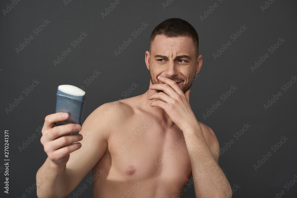 Waist up of Caucasian guy holding male cosmetics for armpits in arm Waist up of Caucasian guy holding male cosmetics for armpits in arm