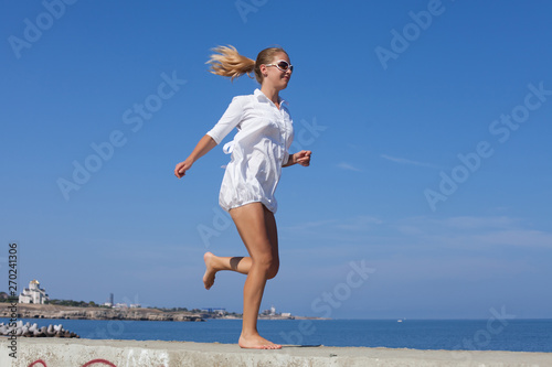 Barefoot girl in white short dress running along breakwater © azazello