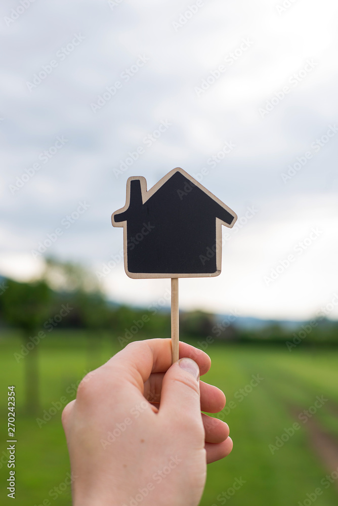 Man is holding the house-shaped little blackboard