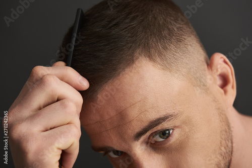 Caucasian guy keeping hairbrush in arm and combing his hair