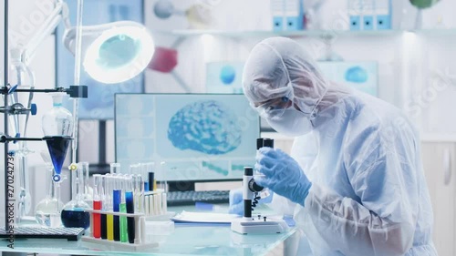 Chemist scientist looking into microscope in modern high end laboratory with 3D scans of brain and DNA on the displays