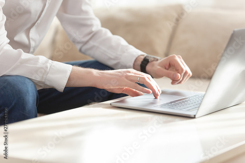 Cute young businessman working remotely using a laptop while sitting on a sofa in his stylish living room in a country house. Remote work concept