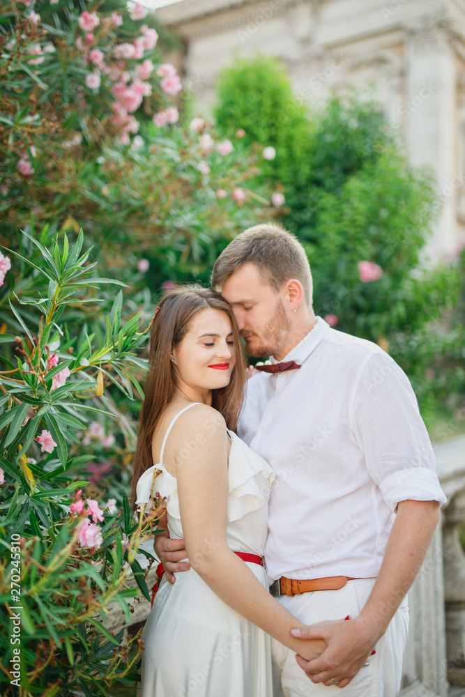 young beautiful couple in white clothes standing near a flowering bush