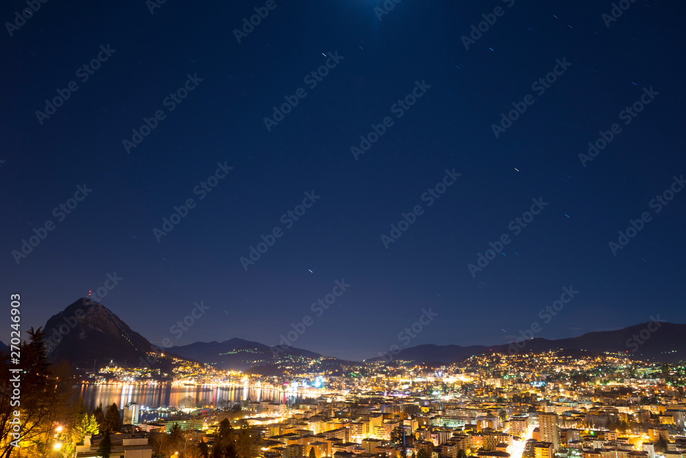 Cityscape at Night with Lake and Mountain and with Star Trails in Lugano, Switzerland.