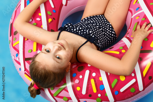 Cute little girl in a bathing suit lying on a donut inflatable circle. The child relaxes on a blue background. Closeup portrait. View from above. © Olga