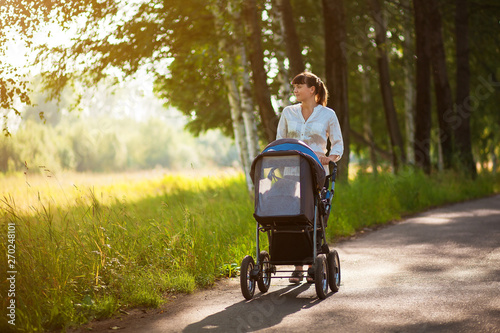 A young mother and a child in a stroller are walking in the park. Walking with the family in nature, in the fresh air photo